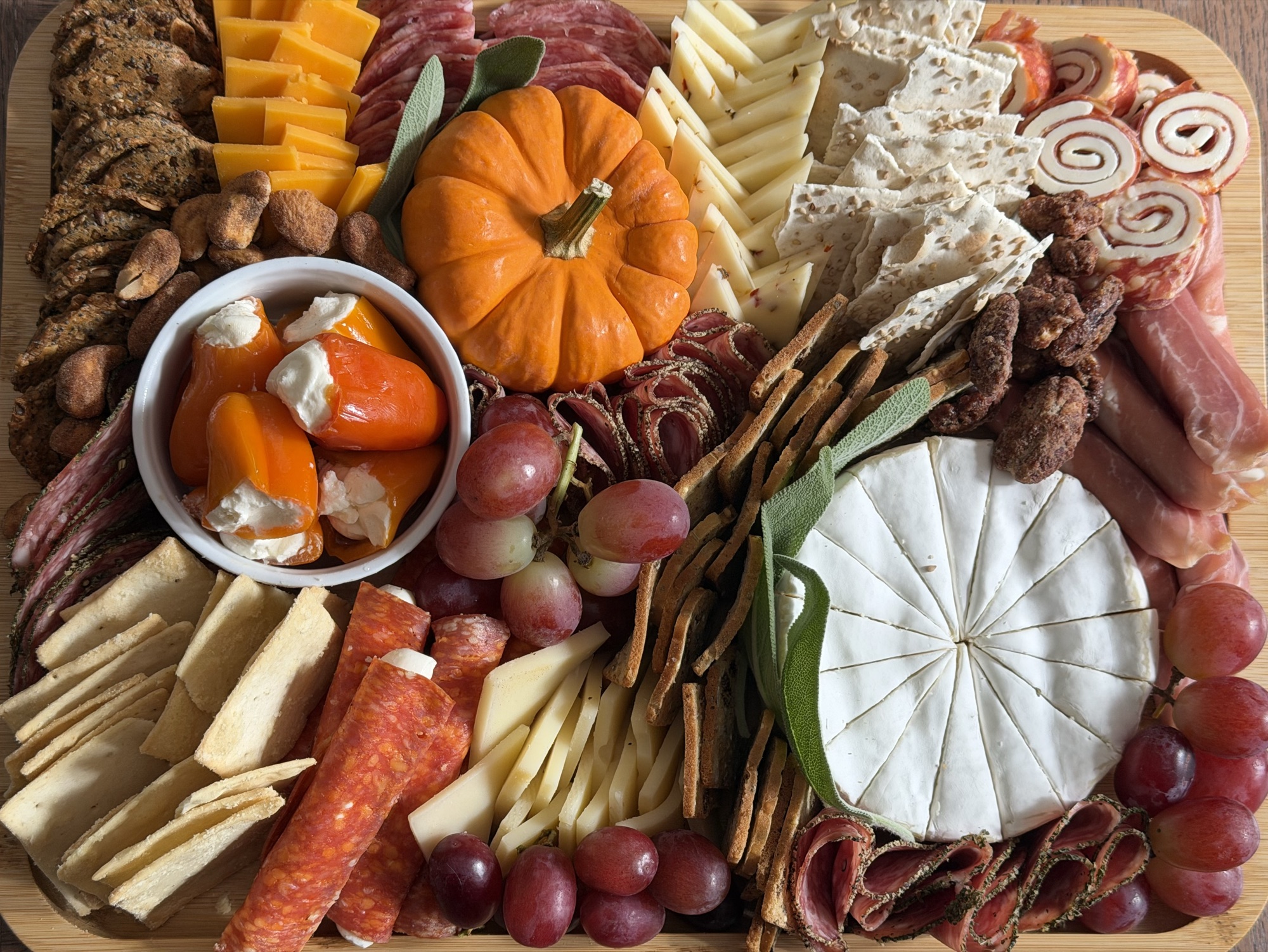 An autumn charcuterie board with cheeses, cured meats, grapes, crackers, and a small pumpkin at the center