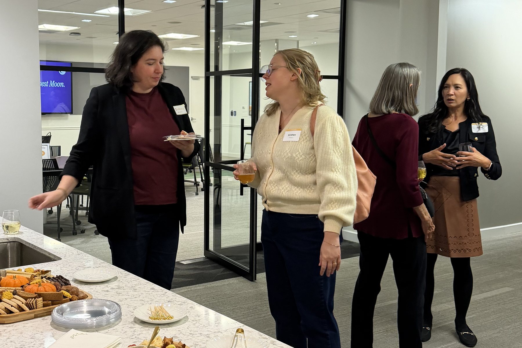 Women talking over drinks beside a counter of autumn charcuterie boards at the Philadelphia Harvest Moon gathering